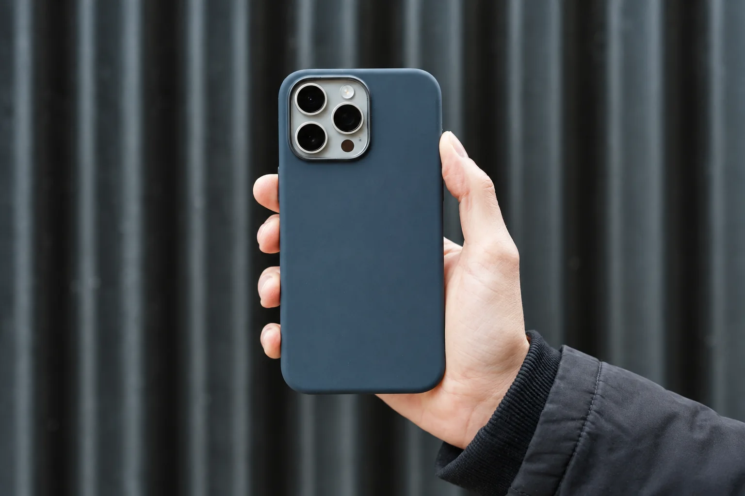 A hand holding a blue-grey phone case against a dark wall.